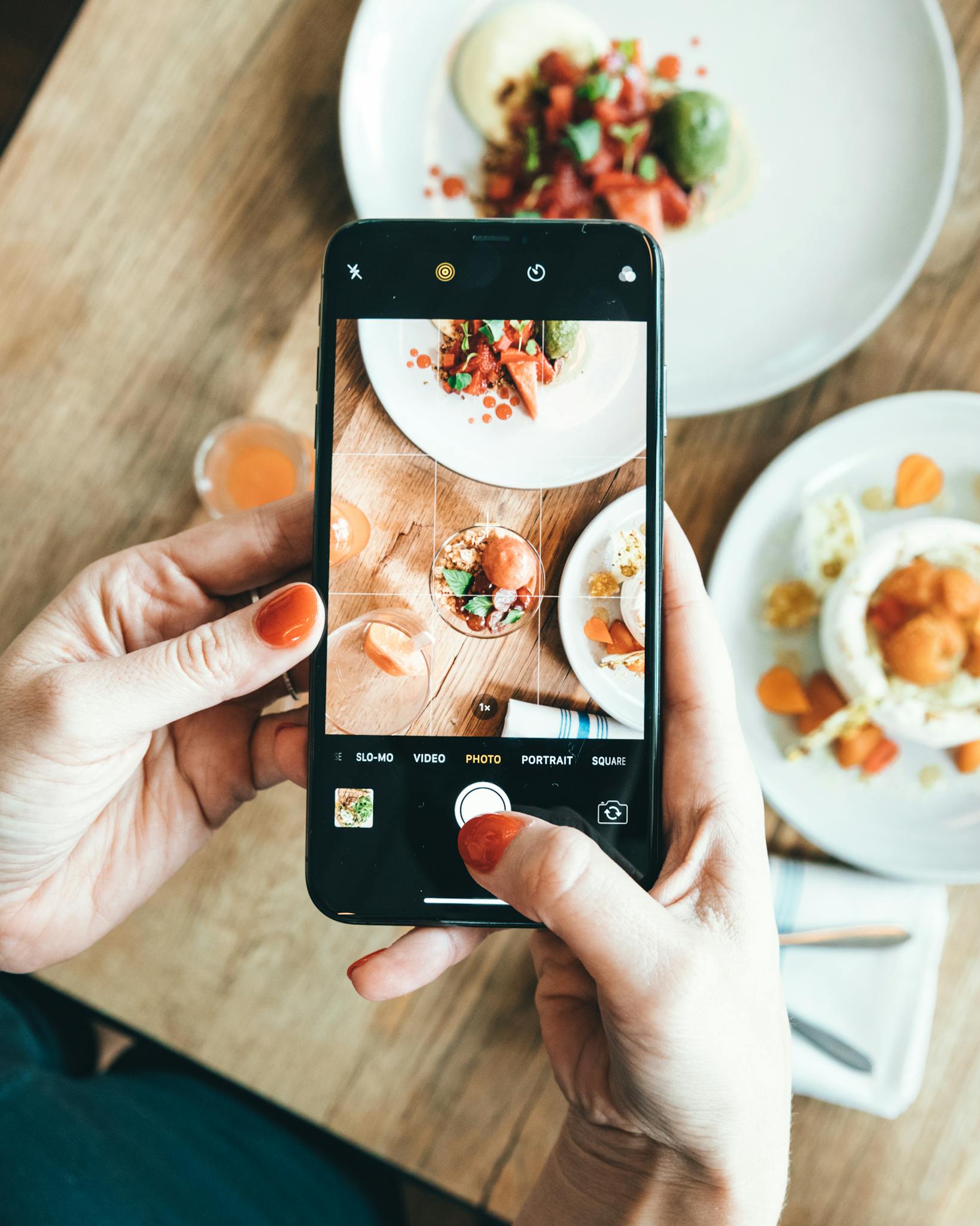 Hands taking photo of delicious plated dishes using a smartphone indoors.